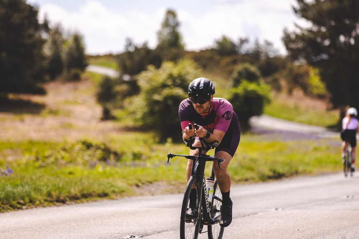 Triathlete in a purple SLS3 tri suit riding a time-trial bike on a country road during training.